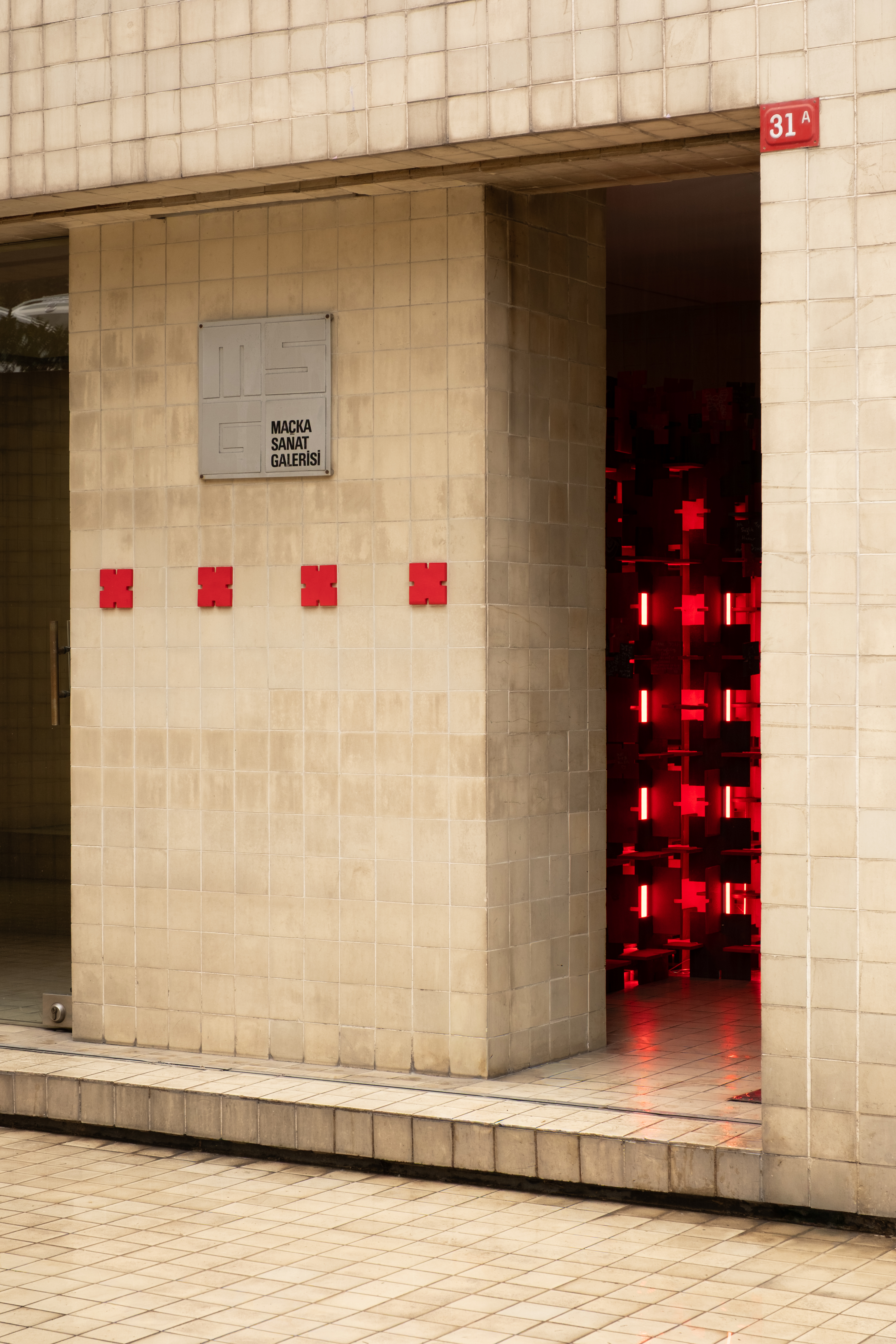 Gallery entrance with a trail of red modules leading inside — Bir Arada installation