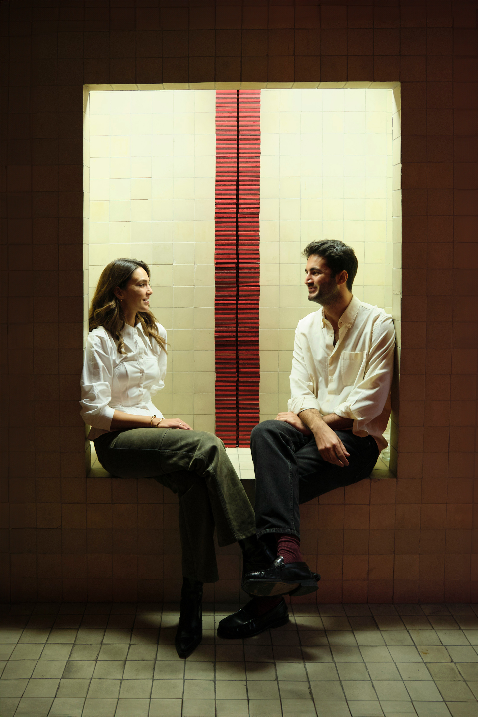 Two visitors seated in a lit niche beside the red column — Bir Arada installation