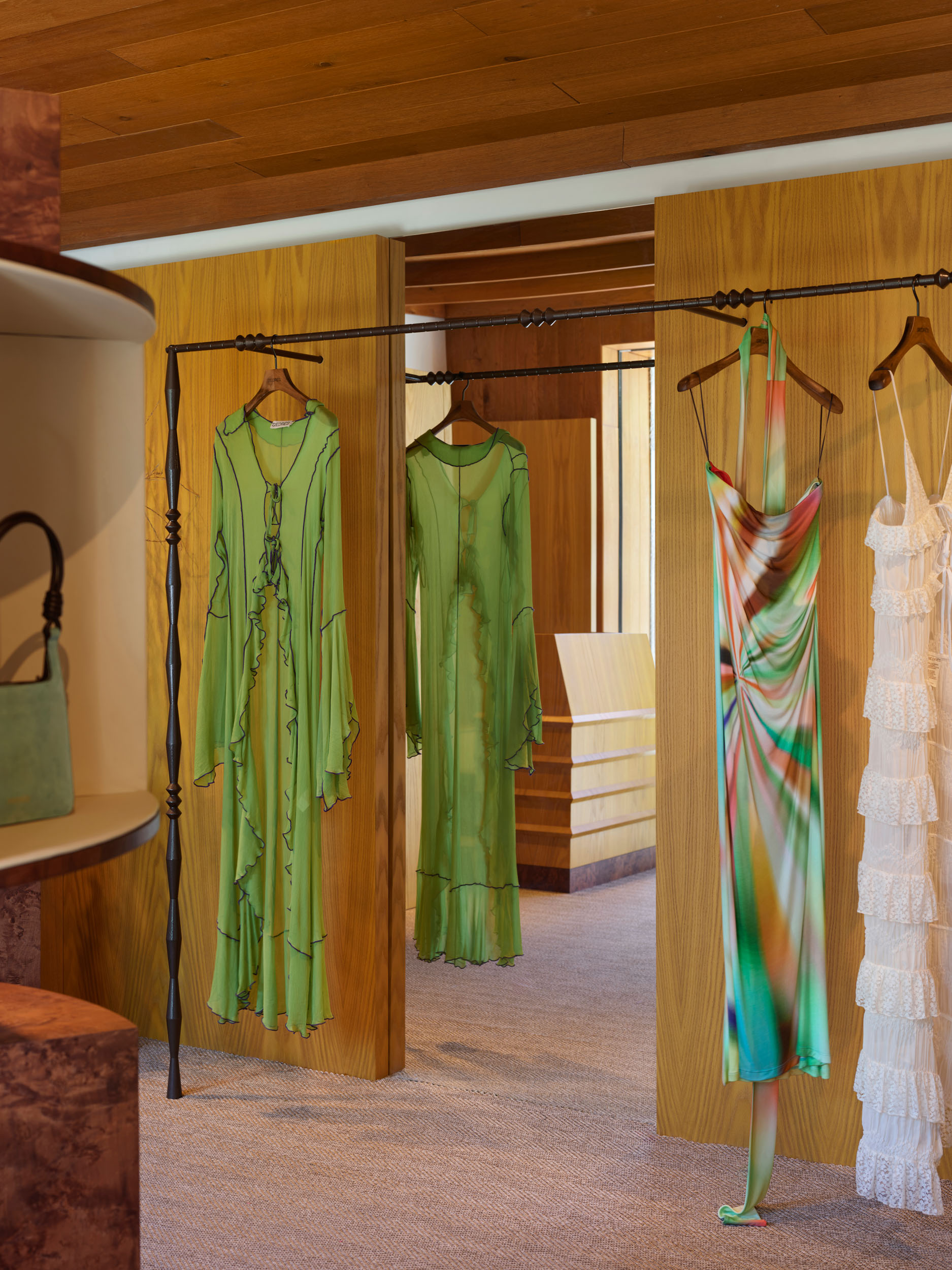 Open wardrobe rails with summer dresses in a warm timber interior — Siedrés retail design
