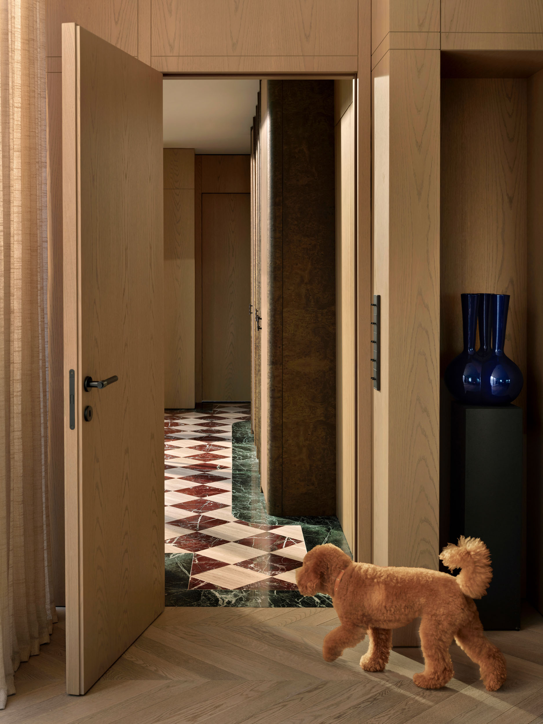 Oak pivot door opening to a patterned marble hallway — Zekeriyakoy TP House